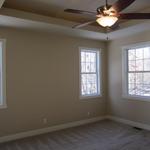 "Master bedroom featuring elegant tray ceilings and several windows for optimal lighting
